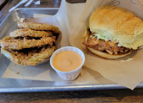 A tray with a fried chicken sandwich and a side of crispy fried pickles with dipping sauce.