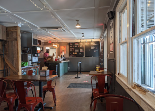 A cozy café interior with wooden tables, red chairs, and a counter in the background. Soft lighting and a welcoming atmosphere.