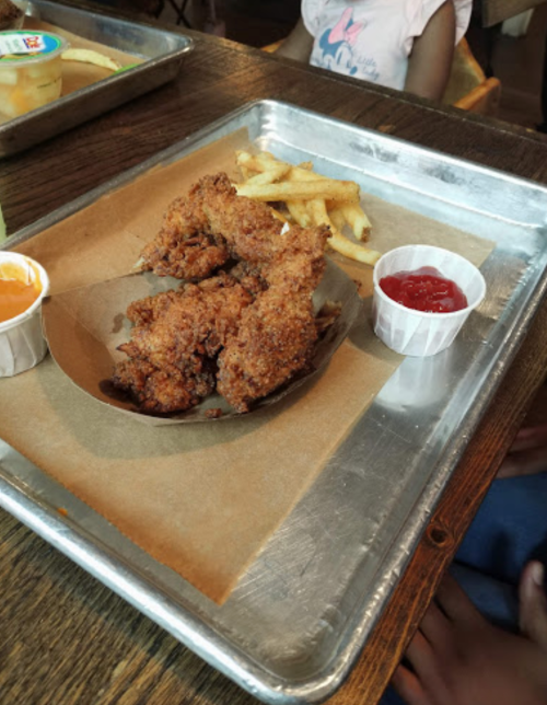 A tray with fried chicken, French fries, a cup of ketchup, and a cup of orange sauce.