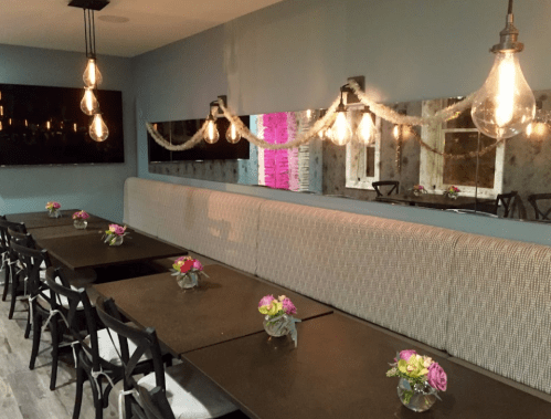 A cozy dining area with a long bench, tables adorned with flowers, and stylish pendant lights.