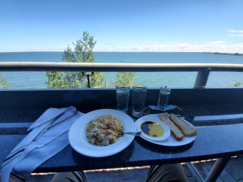 A plate of pasta with bread and olive oil, set on a table overlooking a serene lake and clear blue sky.