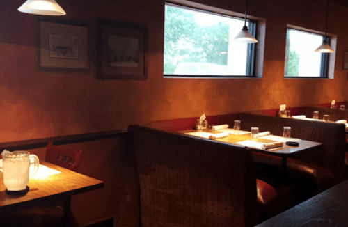 Cozy restaurant interior with wooden tables, booths, and large windows letting in natural light.