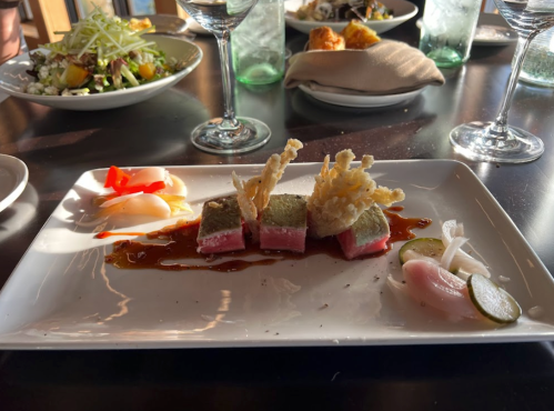 A plate of gourmet sushi with pink tuna, garnished with crispy elements and pickled vegetables, set on a dark table.