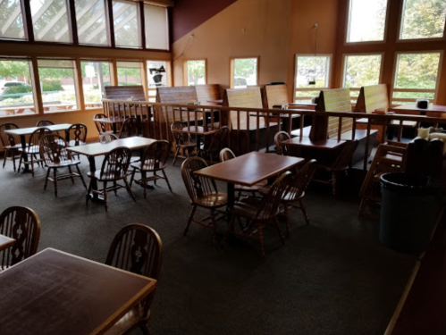 A spacious restaurant interior with wooden tables and chairs, large windows, and a cozy atmosphere.