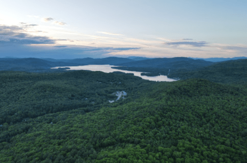 Aerial view of lush green mountains surrounding a serene lake at sunset, with soft clouds in the sky.