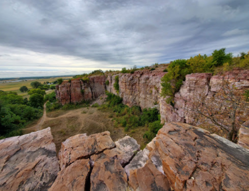 A rocky cliff with greenery below, under a cloudy sky, showcasing a natural landscape.