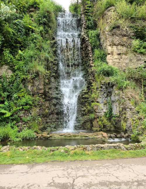 A serene waterfall cascading down rocky cliffs, surrounded by lush greenery and a small pool at the base.