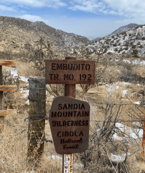 Signpost for Embudito Trail No. 192 in Sandia Mountain Wilderness, Cibola National Forest, surrounded by a dry landscape.