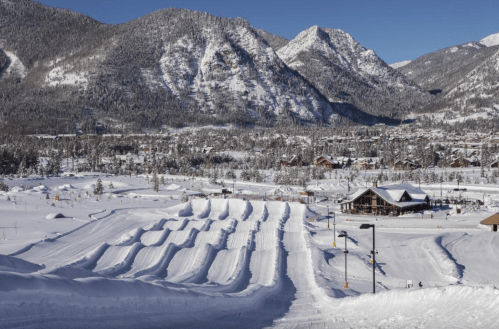 Snow-covered landscape with ski slopes and mountains in the background under a clear blue sky.