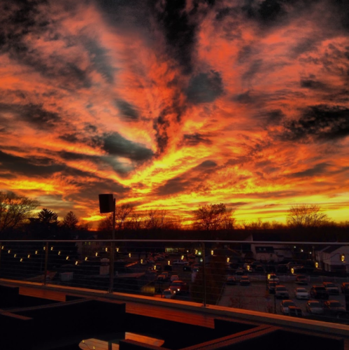Vibrant sunset with dramatic clouds in shades of orange and pink, viewed from a rooftop with string lights.