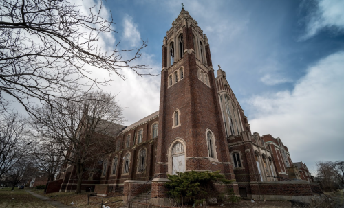 A tall brick church with a tower, surrounded by bare trees under a cloudy sky.