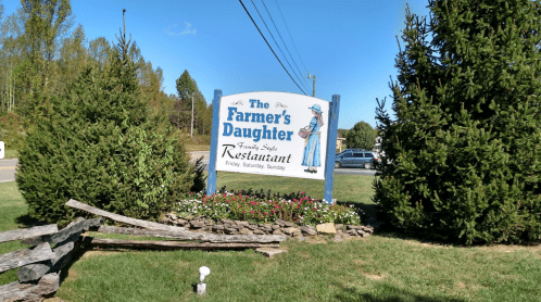 Sign for "The Farmer's Daughter" restaurant, featuring a woman in blue and surrounded by greenery and flowers.