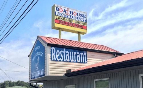 Sign for "Cooks' Boathouse Restaurant" with a lakeside dining theme, featuring a blue and white color scheme.