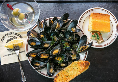 A plate of mussels with lemon, garlic bread, a slice of cornbread, and a martini with olives on the side.