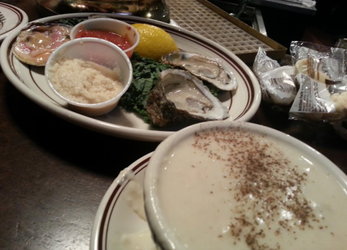 A plate with oysters on the half shell, condiments, and a bowl of clam chowder garnished with pepper.