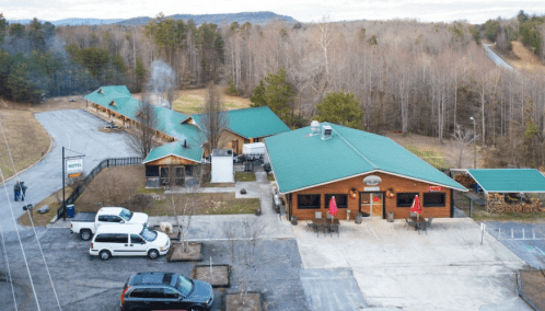 Aerial view of a rustic lodge with green roofs, surrounded by trees and a gravel parking area.