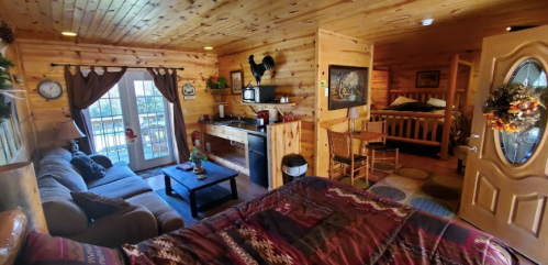 Cozy wooden cabin interior with a bed, seating area, kitchenette, and balcony access, decorated with rustic accents.