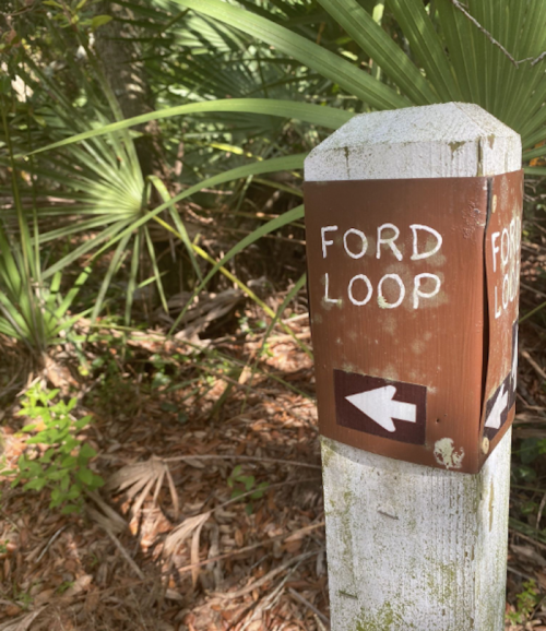 Signpost indicating the direction to Ford Loop, surrounded by lush greenery and palm leaves.