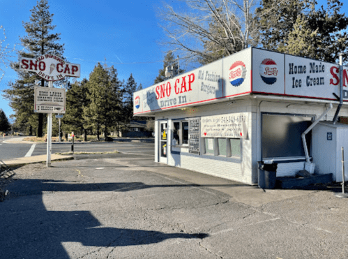 A small drive-in restaurant named "Sno Cap" with a sign, featuring homemade ice cream, surrounded by trees.