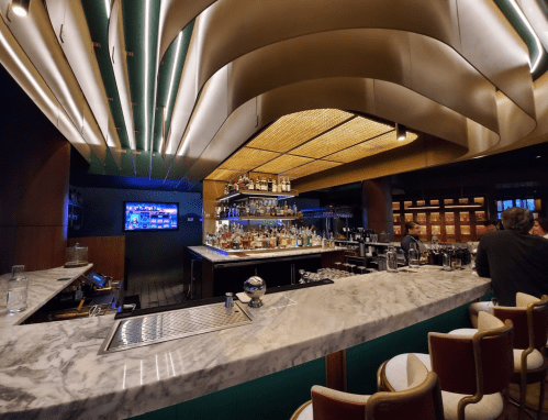 A stylish bar with a marble countertop, shelves of liquor, and modern lighting in a sleek interior setting.
