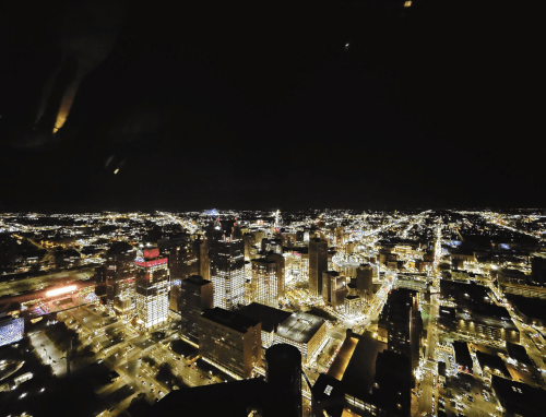 Aerial view of a city skyline at night, illuminated by countless lights against a dark sky.