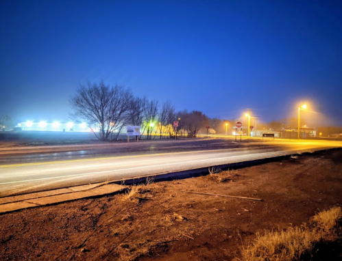 A dimly lit road at night with streetlights and trees in the background, creating a serene, quiet atmosphere.