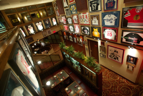 Interior of a restaurant featuring walls adorned with framed sports jerseys and memorabilia, with dining tables below.