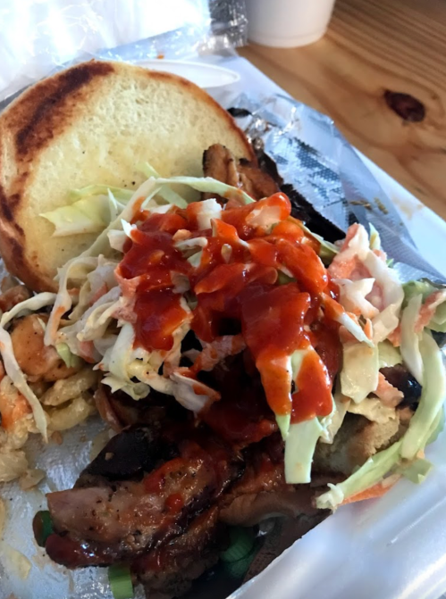A close-up of a sandwich with grilled meat, coleslaw, and sauce on a bun, served in a takeout container.