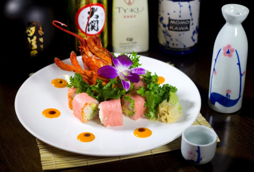 A beautifully arranged sushi plate featuring lobster, colorful rolls, lettuce, and a decorative flower.