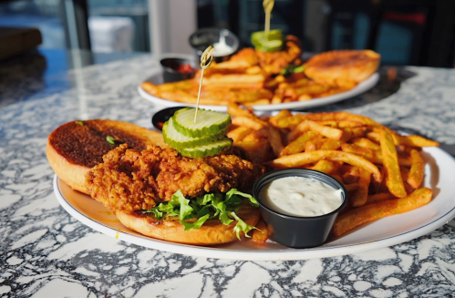 A plate featuring a fried chicken sandwich with pickles, lettuce, and fries, served with a side of dipping sauce.