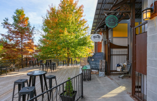 Outdoor seating area of a café with wooden deck, black stools, and colorful autumn trees in the background.