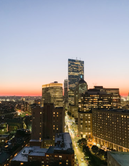 City skyline at dusk, featuring tall buildings and a gradient sky transitioning from orange to deep blue.