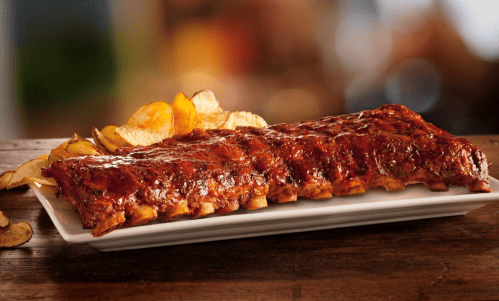 A platter of glazed ribs served with crispy potato chips on the side, set on a wooden table.