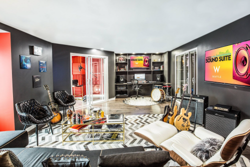 A stylish music studio with guitars, a drum set, and modern decor, featuring soundproofing and large screens.