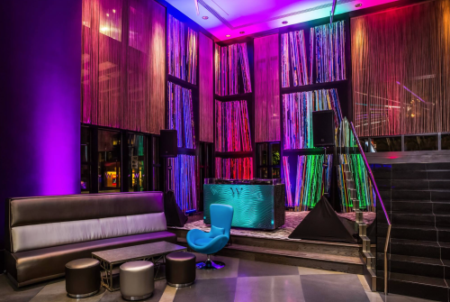 A modern lounge with colorful lighting, a sleek bar, and stylish seating arrangements.
