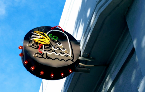 A circular neon sign with colorful wires and lights, mounted on a building against a blue sky.