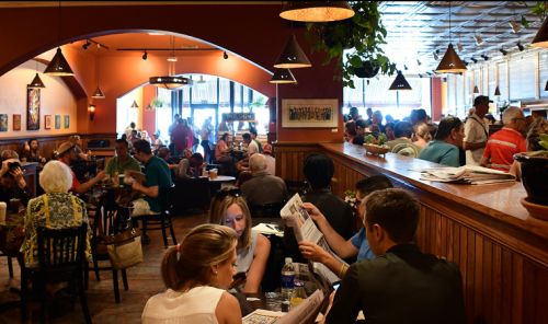 A busy café filled with people dining, chatting, and reading menus in a warm, inviting atmosphere.