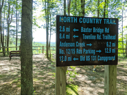 Signpost for North Country Trail with distances to various locations, surrounded by trees and a scenic view in the background.