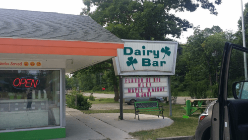 A Dairy Bar with a sign featuring "Maple Walnut" as the flavor of the week, surrounded by trees and an open sign.