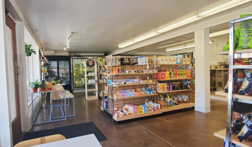 Interior of a grocery store featuring shelves stocked with various food items and a cooler in the background.