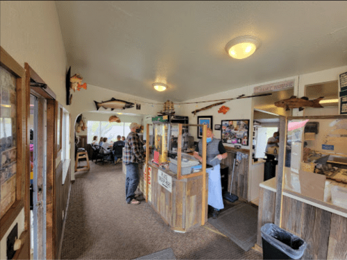 A cozy restaurant interior with a counter, customers, and fishing-themed decor on the walls.