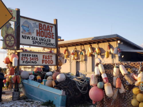 A sign for "The Boat House" with fishing gear and colorful buoys in front of a building, indicating sportfishing and fast food.