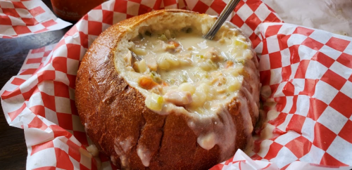 A bread bowl filled with creamy soup, served in a red and white checkered paper basket.