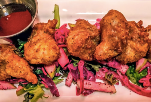 Crispy fried chicken pieces served on a bed of colorful slaw with a side of dipping sauce.