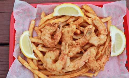 A red tray filled with golden fries and crispy fried shrimp, garnished with lemon wedges.