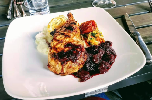 Grilled chicken leg served with mashed potatoes, sautéed vegetables, and a berry sauce on a white plate.