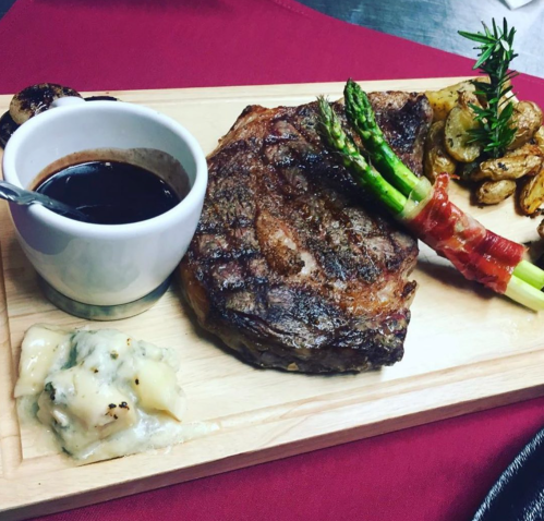 A beautifully plated steak with asparagus, roasted potatoes, and a side of sauce on a wooden board.