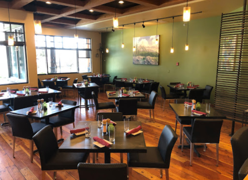 A spacious restaurant with wooden floors, black tables set for dining, and large windows letting in natural light.