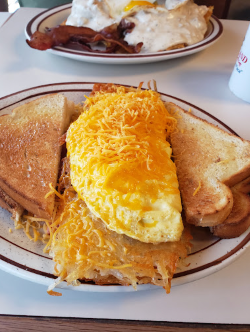 A cheesy omelet served on toasted bread with crispy hash browns, alongside a plate of bacon and gravy.