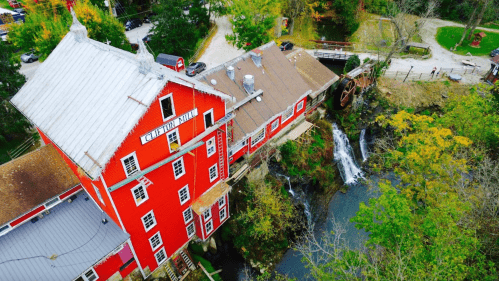 Aerial view of a red barn-like building next to a small waterfall and lush greenery.